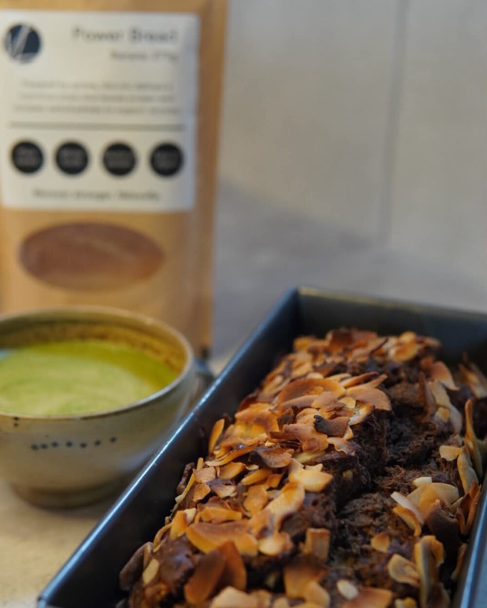 A Verdant Life Power Bread loaf topped with toasted coconut, beside a matcha.
